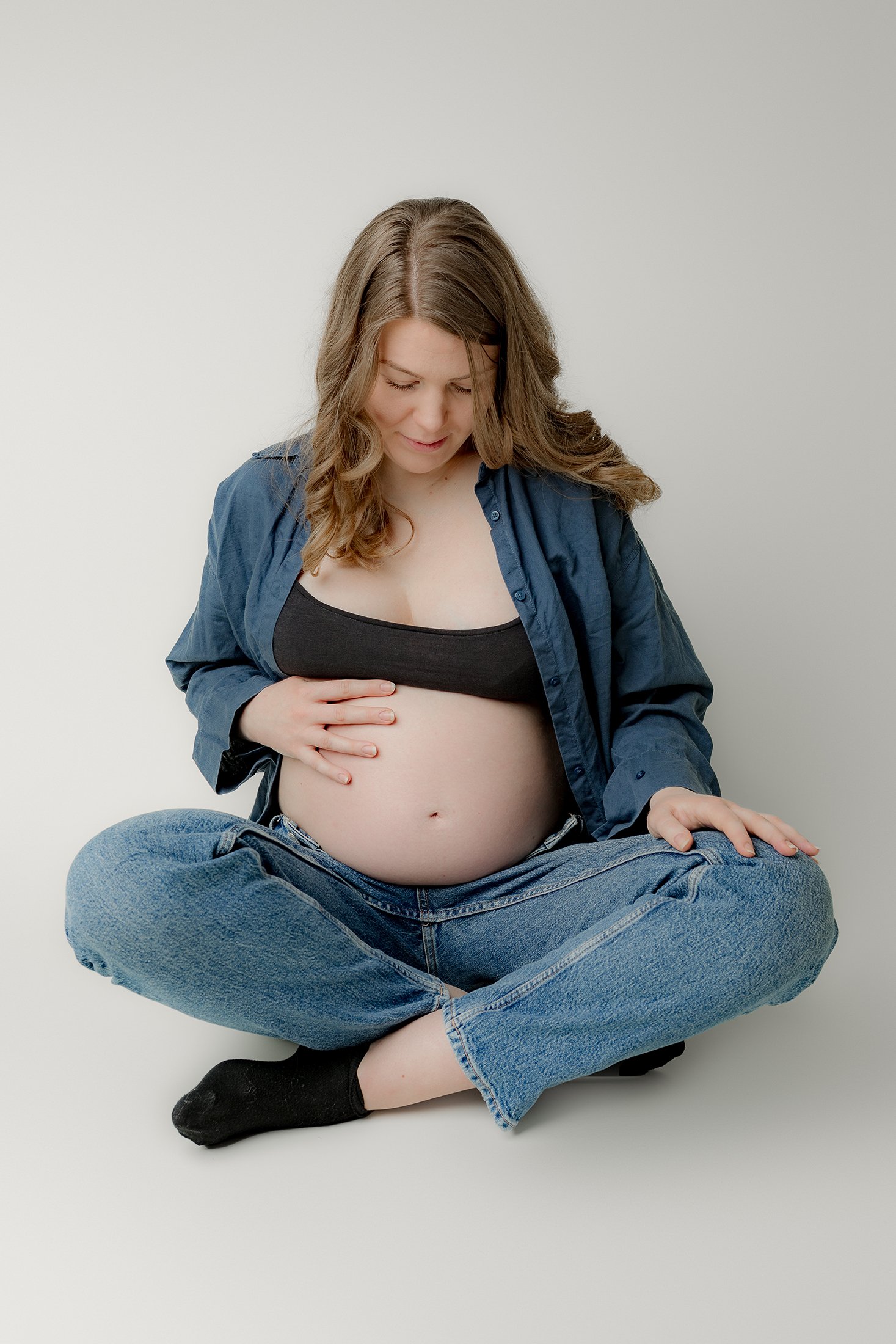Odottava äiti istuu lattialla jalat risti-istunnassa. Päällään sininen paitapusero ja farkut, käsi vatsan päällä.