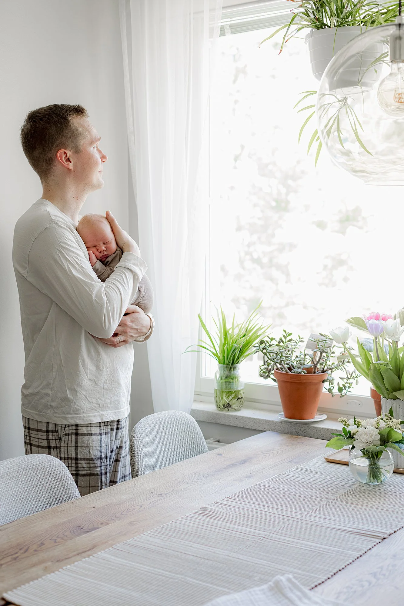 Isä seisoo ikkunan edessä, katsoo ulos ja pitää rintaansa vasten vastasyntynyttä. 