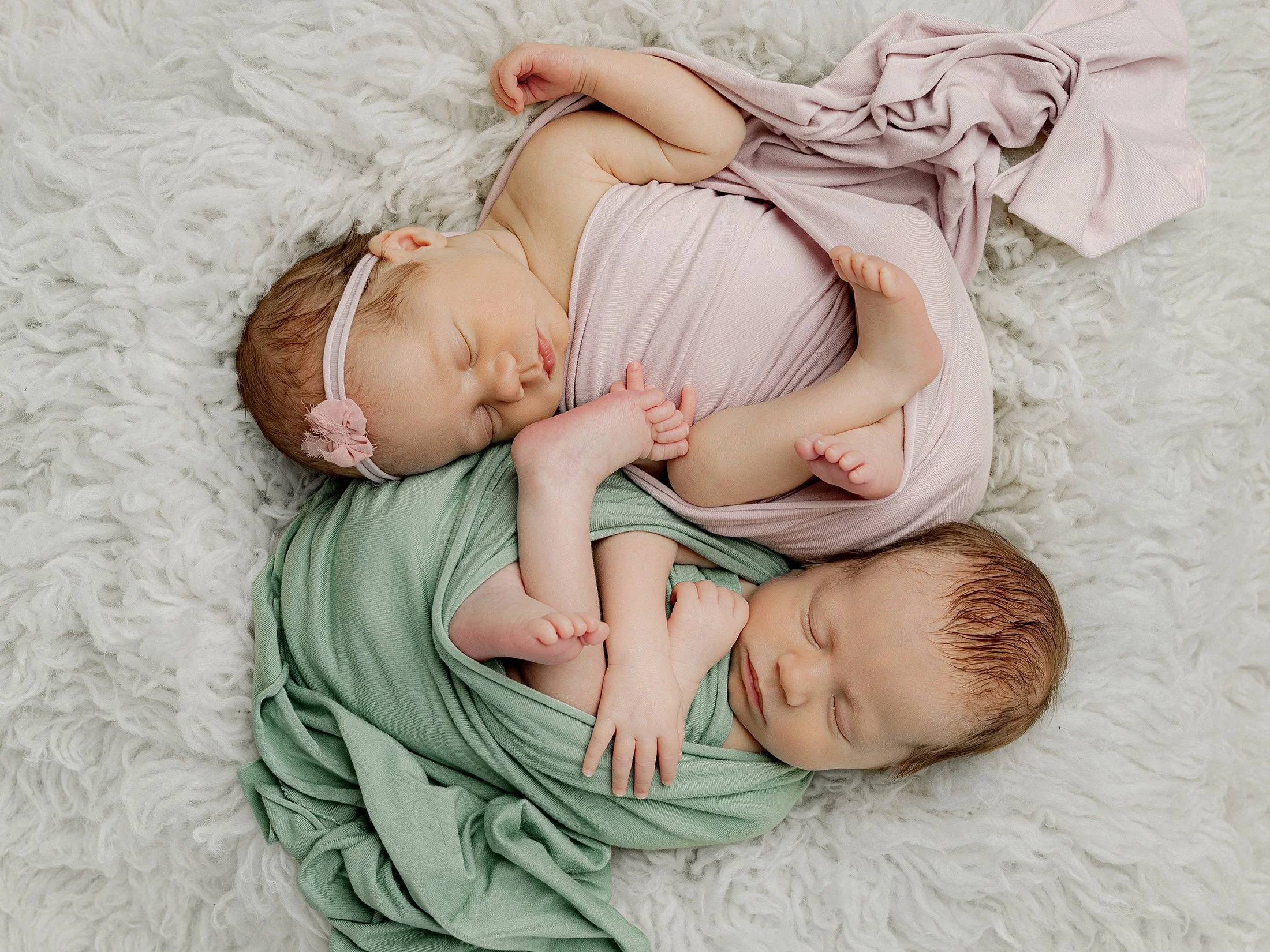 Kaksosvauvat kapaloituna vierekkäin, toisella vihreä ja toisella vaaleanpunainen kapalo