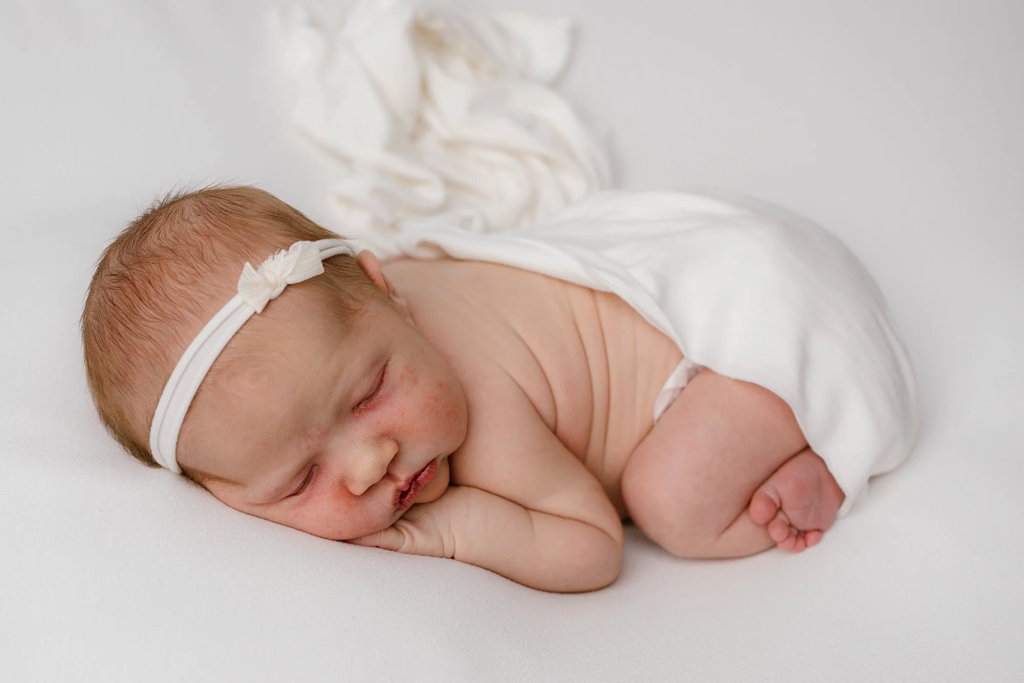 Vastasyntynyt vauva makaa vatsallaan, valkoinen patja ja päässä valkoinen pieni rusetti