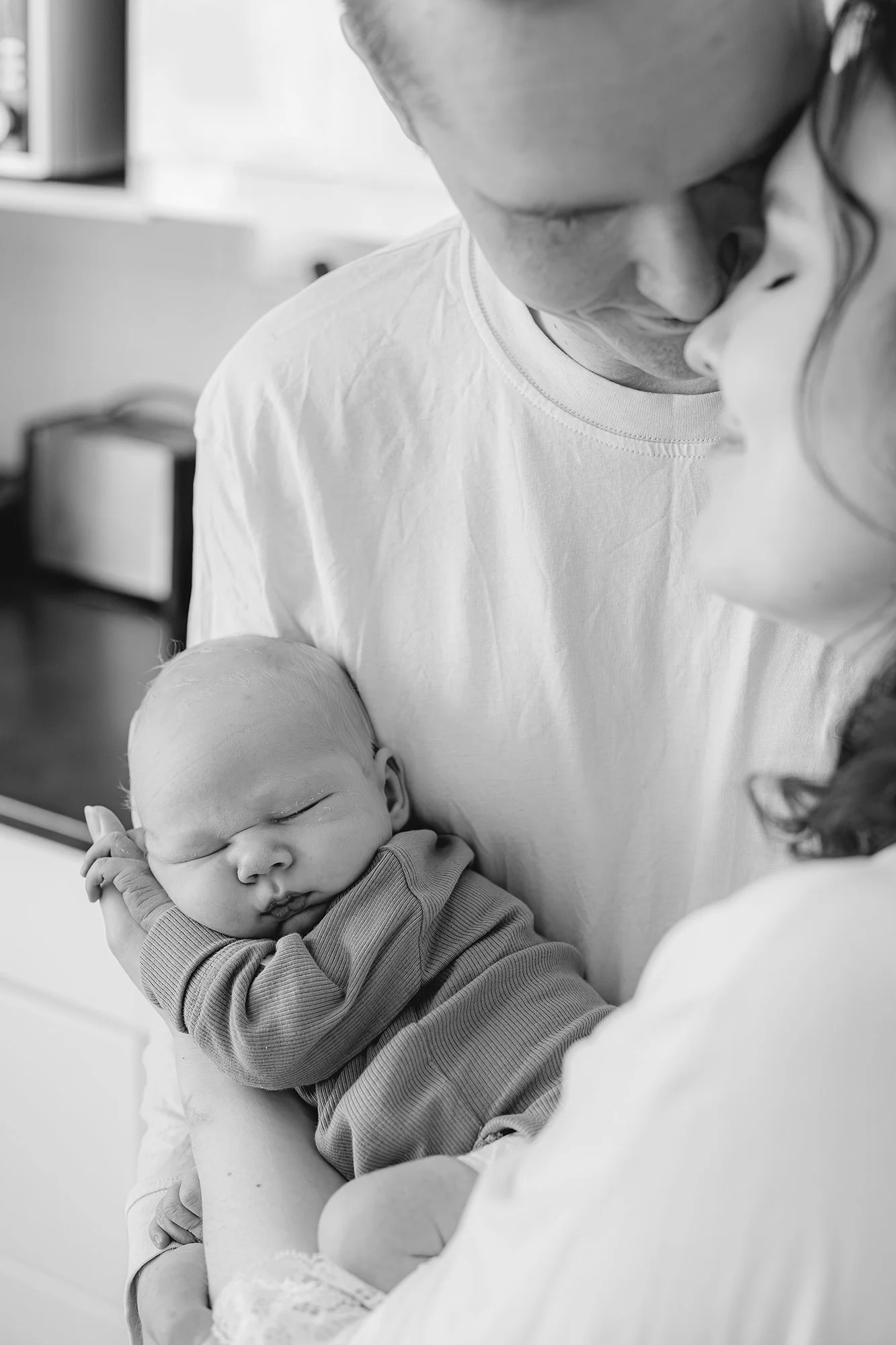 Äiti ja isä pitelevät hellästi vastasyntynyttä vauvaa toisiinsa painautuen.