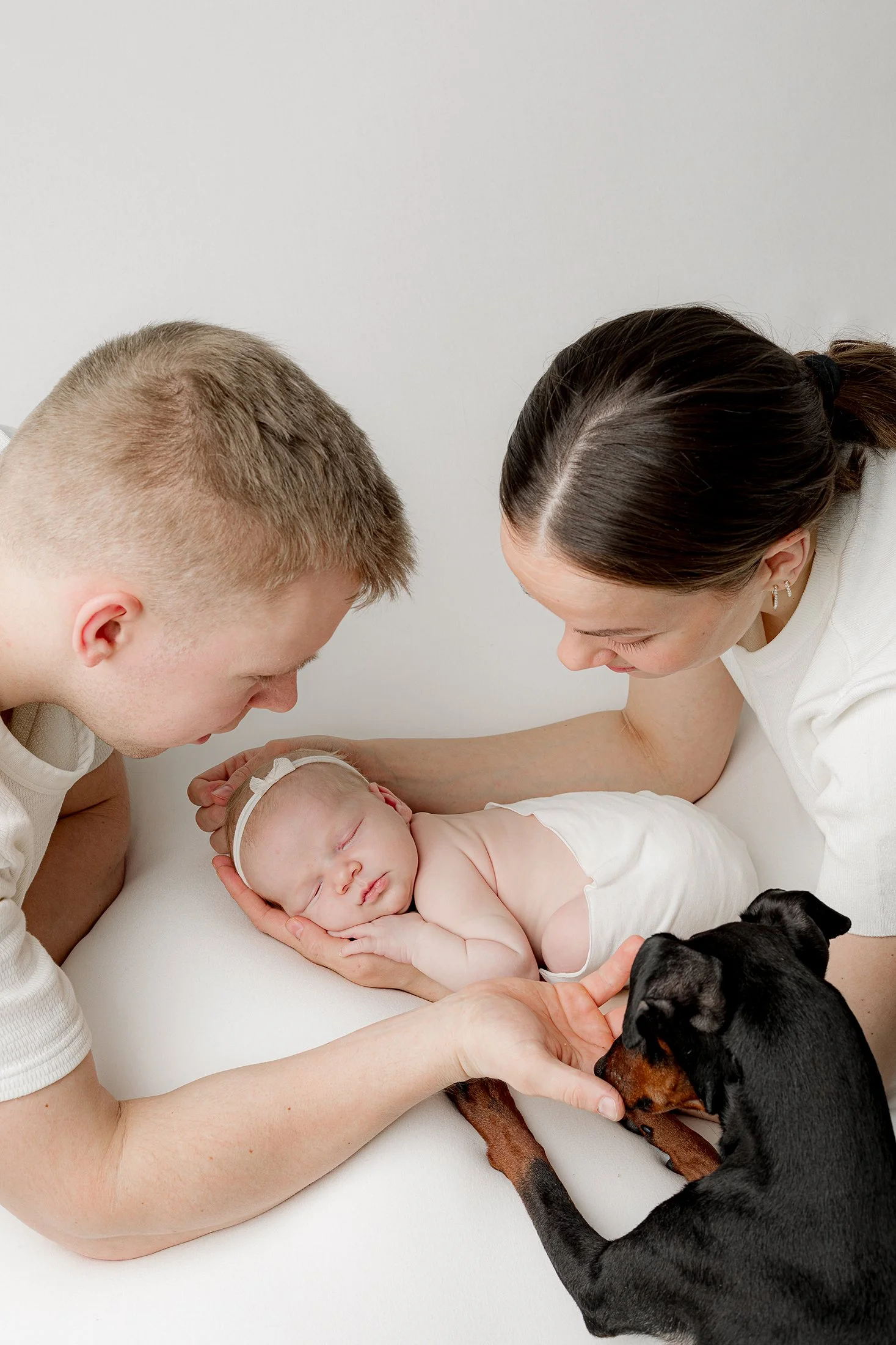 Äiti ja isä vastasyntyneen ympärillä, perheen koira kurkistaa vierellä