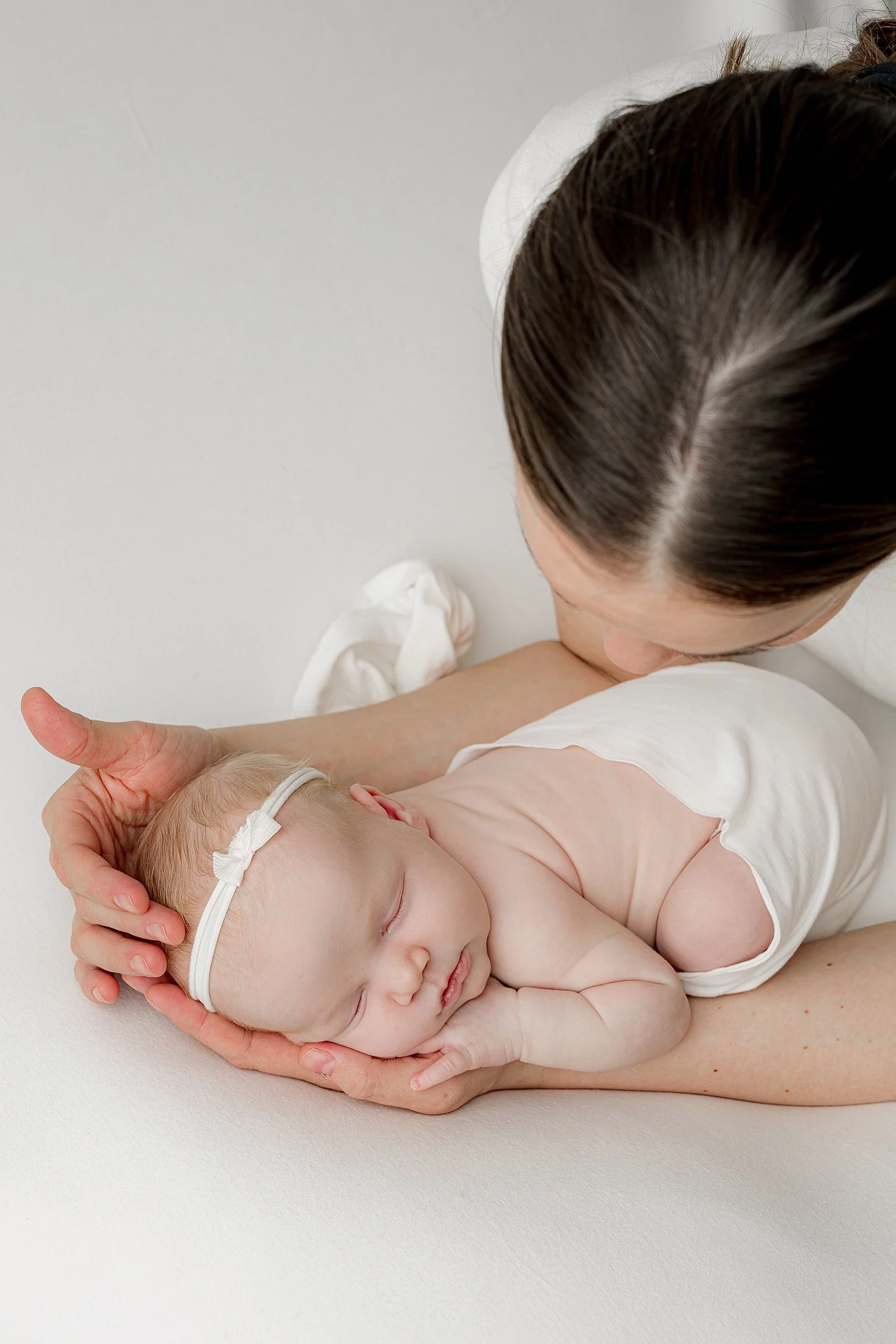 Äiti pitää hellästi vastasyntynyttä vauvaa joka on kapaloitu valkoiseen kankaaseen.