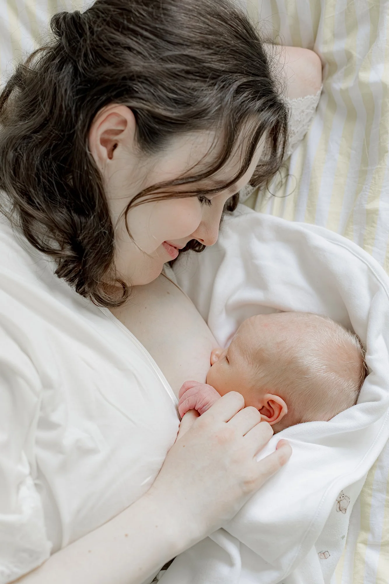 Äiti pitää rintaansa vasten vastasyntynyttä, makoilevat vuoteella.