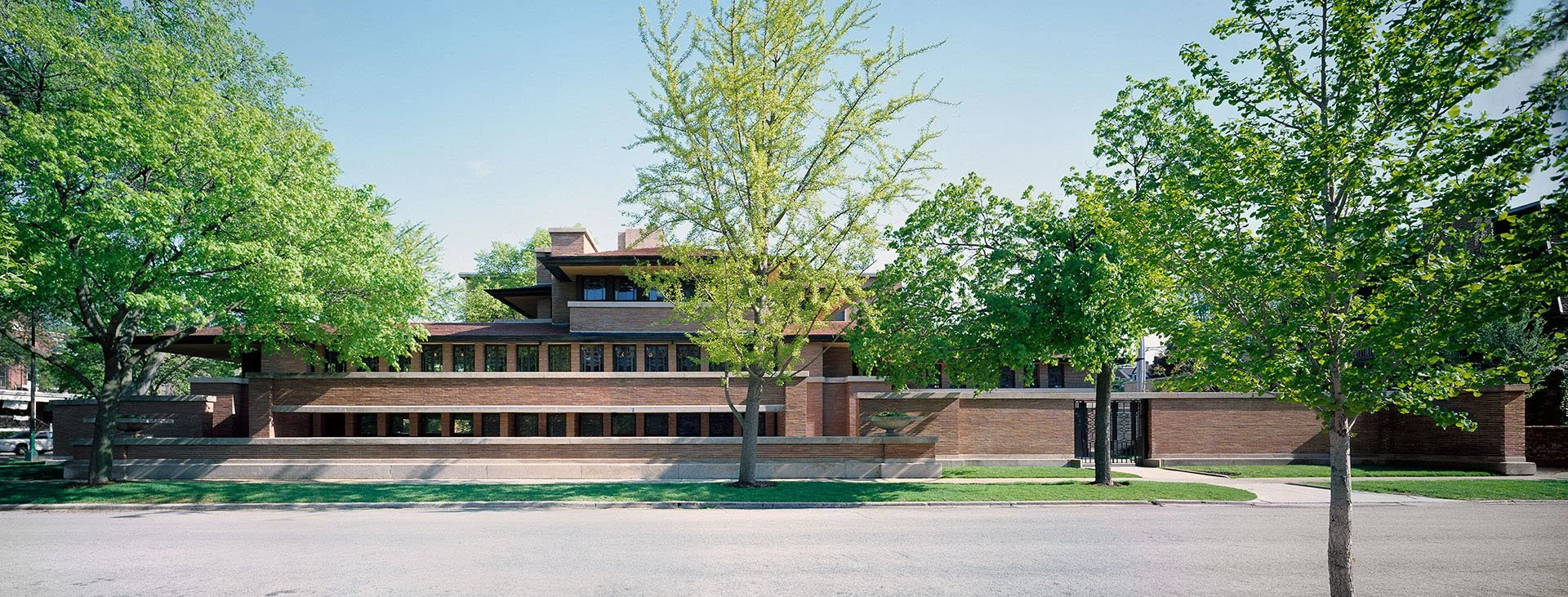 Modern multi-story house with brick exterior, surrounded by green trees, on a sunny day.