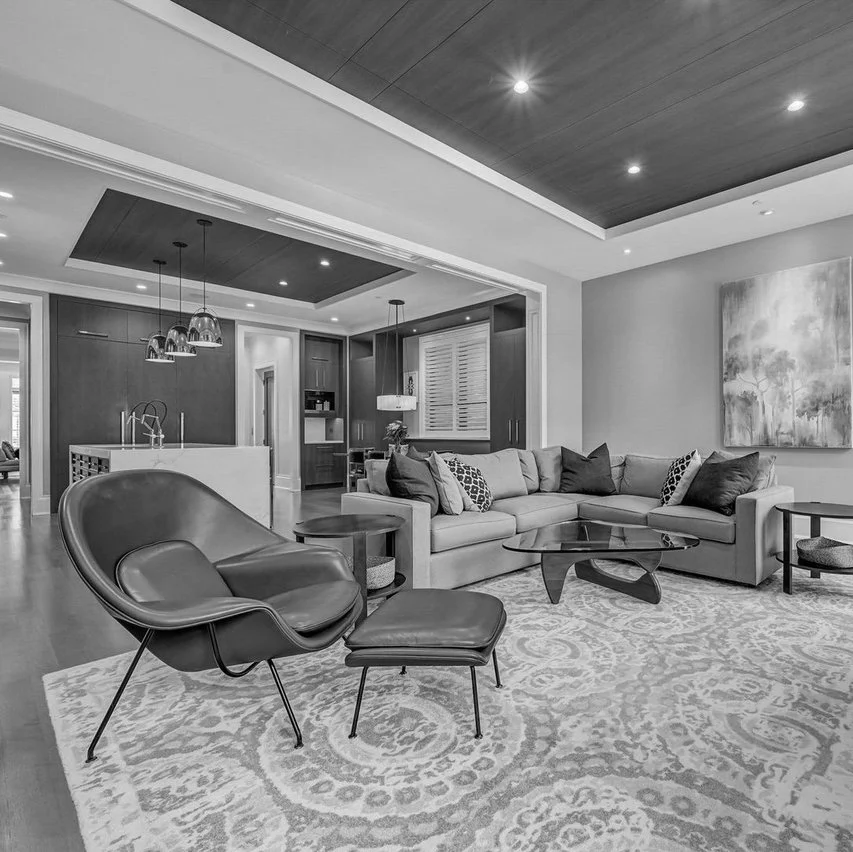 Modern living room with a large sectional sofa, a contemporary armchair with an ottoman, and a glass coffee table on a patterned rug.