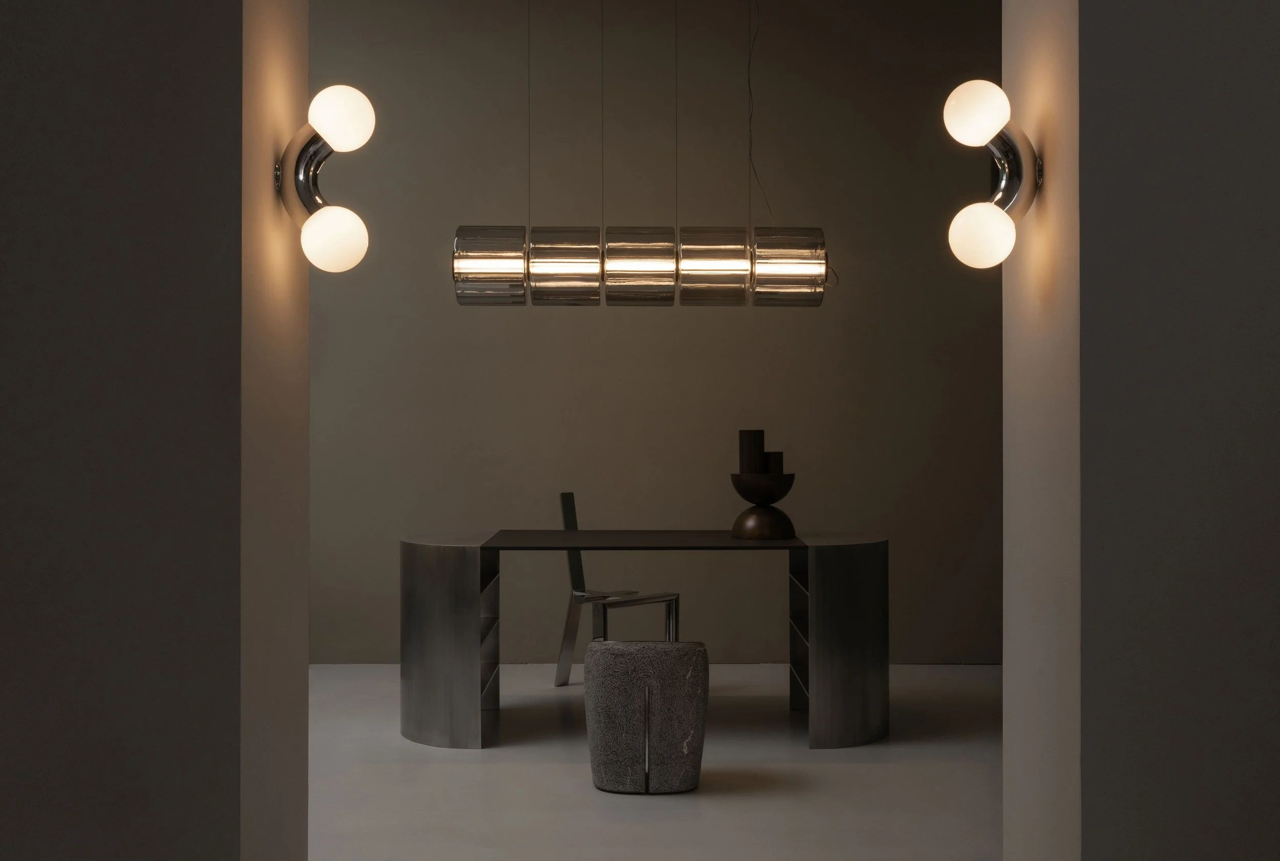 Minimalist interior with a dark desk, modern chair, decorative objects, and top and side wall lights.