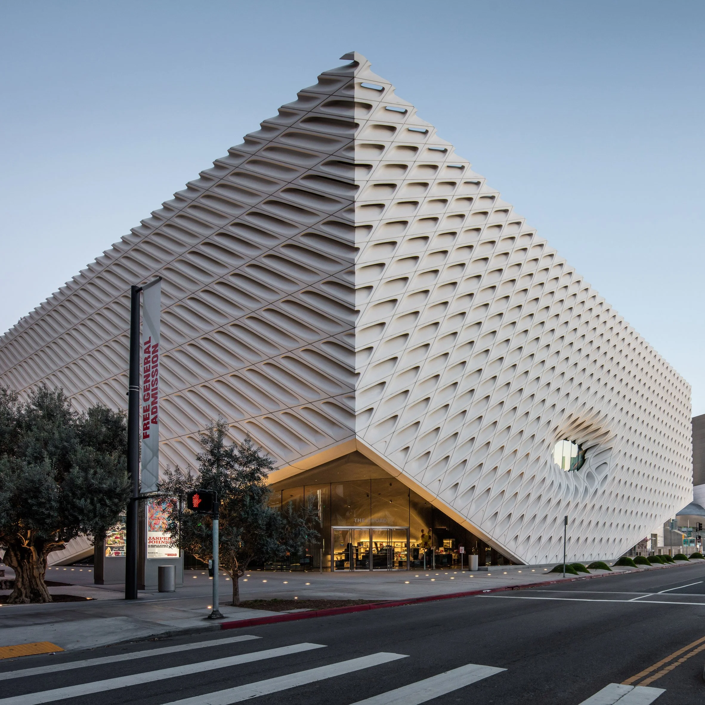Modern building with a distinctive, honeycomb-like facade, featuring a circular window and a street view with trees and pedestrian crosswalk.