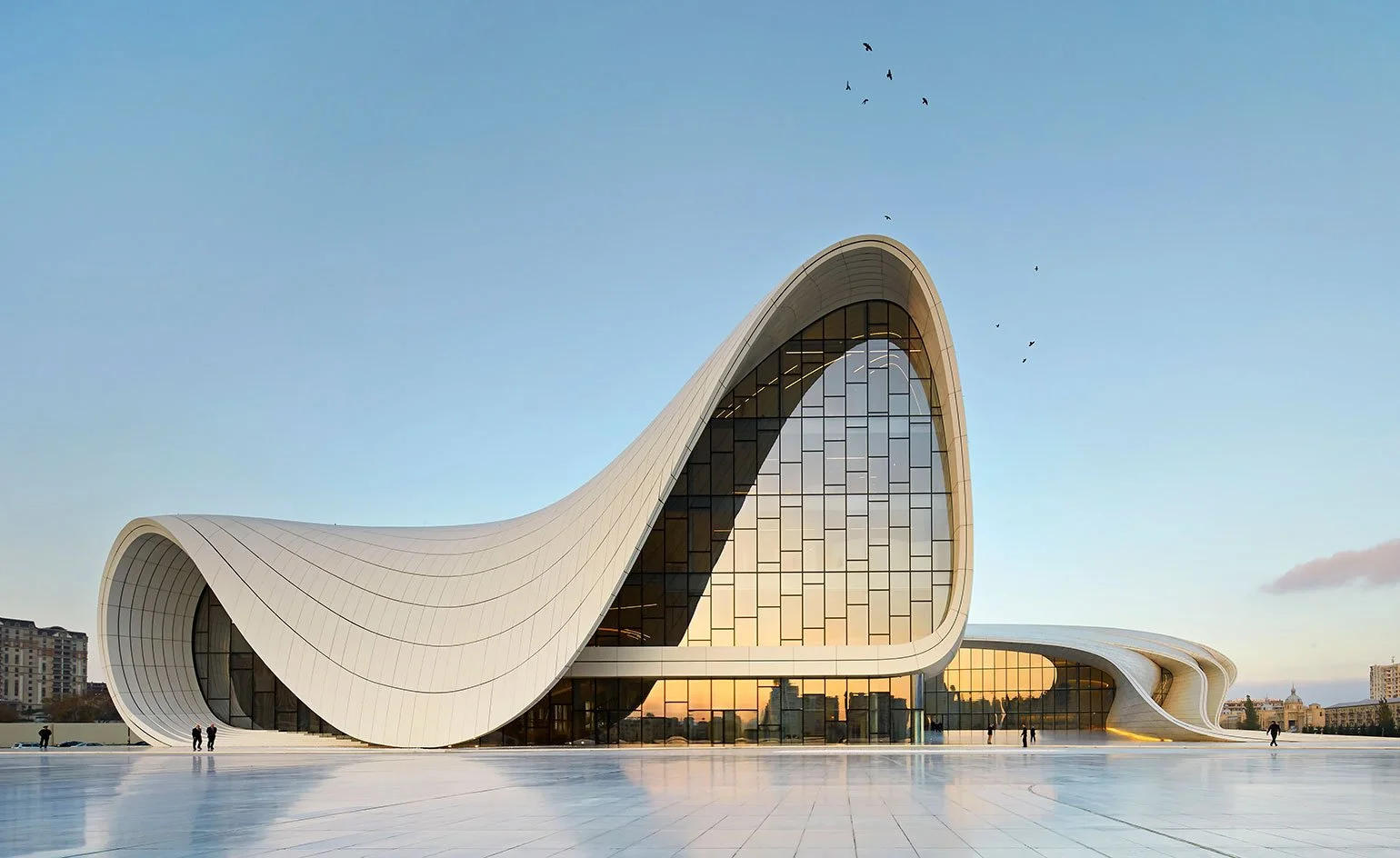 Modern architectural building with flowing white curves and large glass windows, with a clear sky and birds flying above.