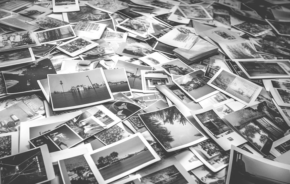 A large collection of scattered photographs and postcards in black and white on a flat surface.