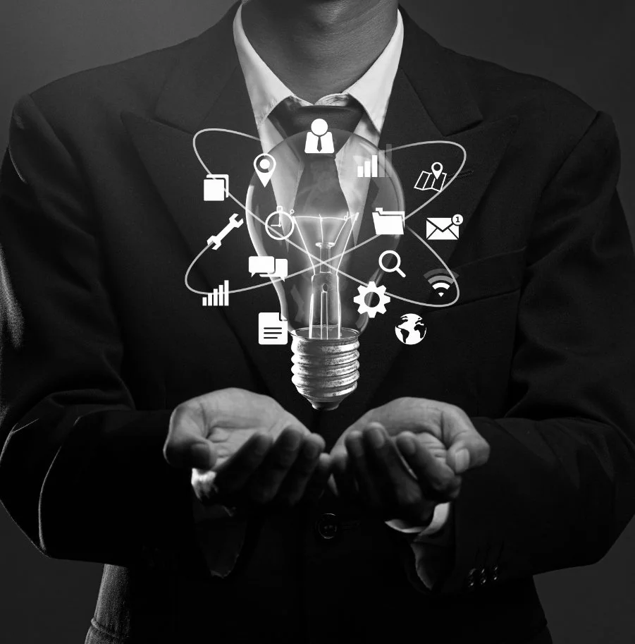 A person in a business suit holding a lightbulb with digital icons representing technology, communication, and data surrounding it.