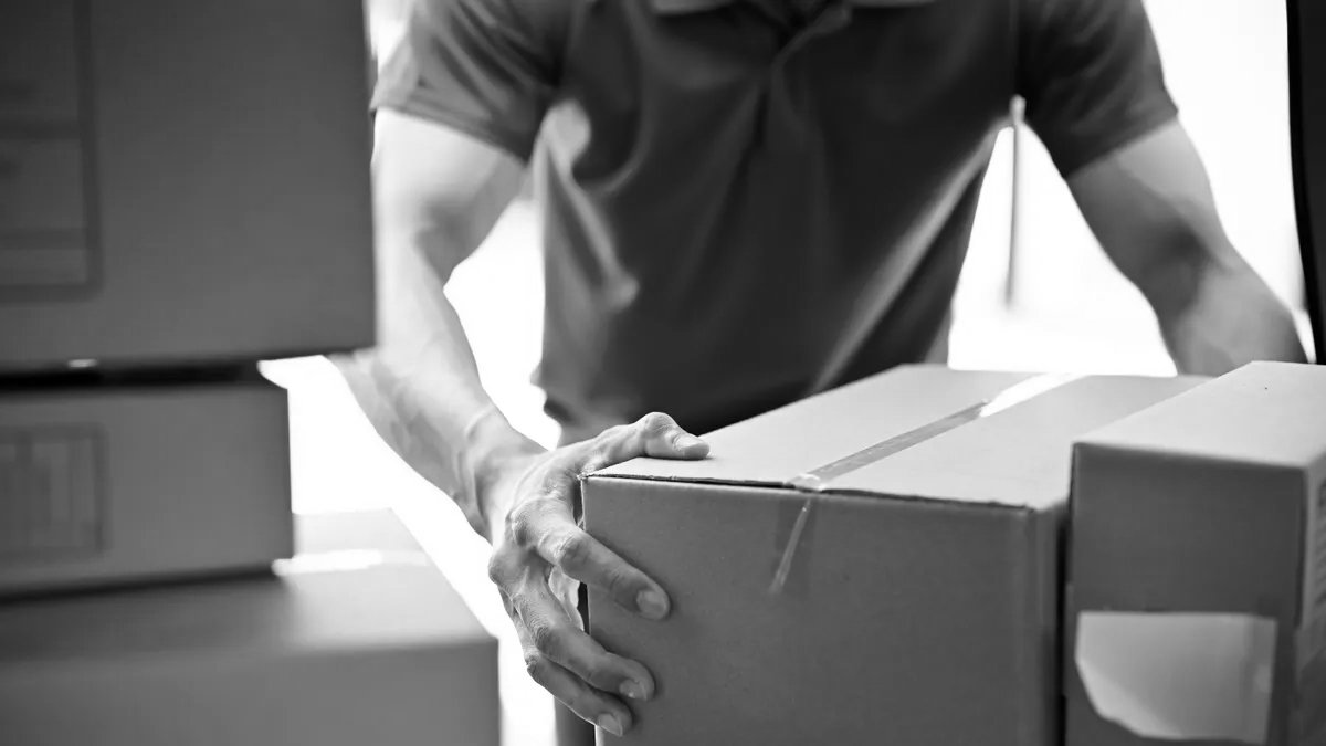 A person handling a cardboard box among other stacked boxes.