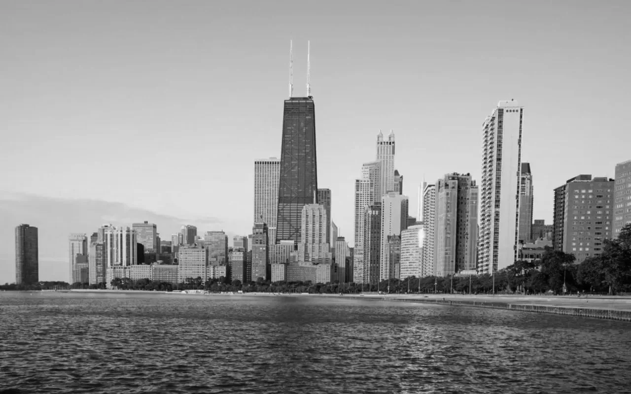 Black and white photo of the Chicago skyline with tall skyscrapers, including the John Hancock Center, along Lake Michigan.