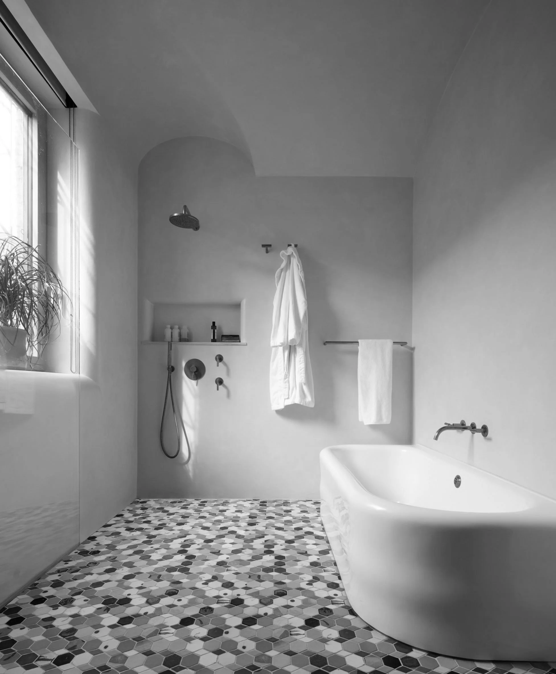 Modern bathroom with bathtub, showerhead, towel rack, and window, in grayscale.