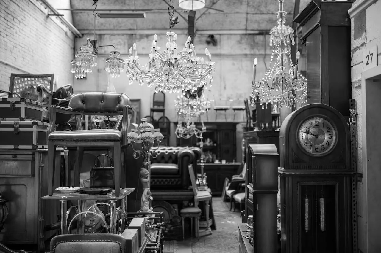 A black and white photo of an antique store filled with vintage furniture, chandeliers, and various decorative items.