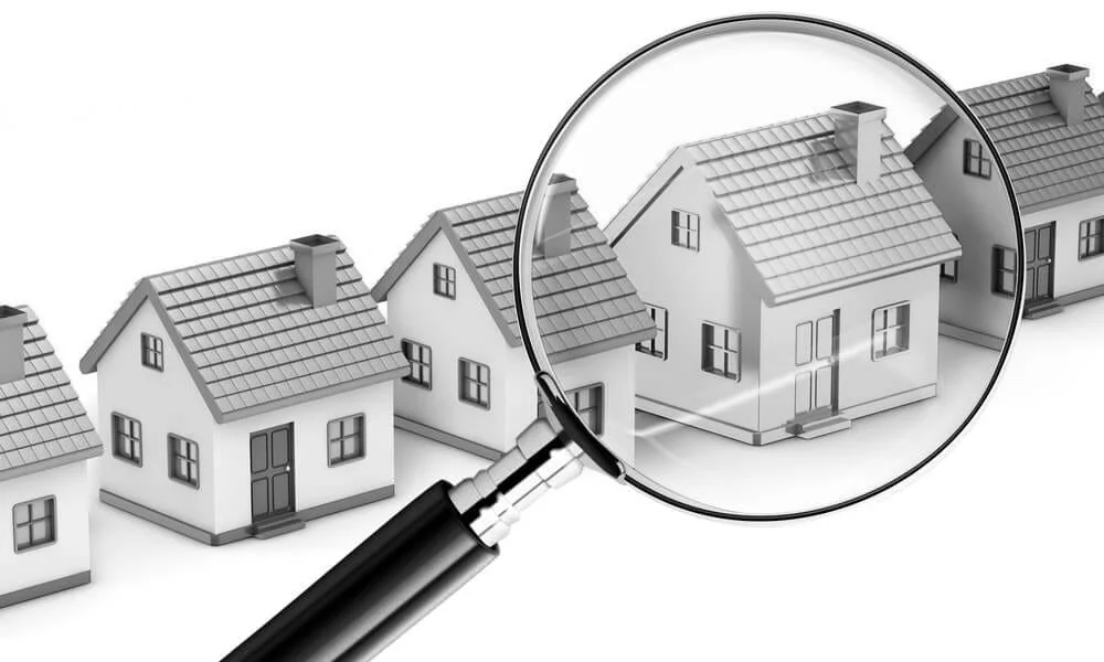 Series of small model houses with a magnifying glass focusing on one house, indicating inspection or selection.