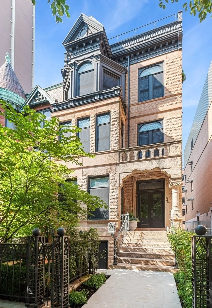 A historic multi-story brownstone building with ornate architectural details and a small front garden, located in an urban setting.