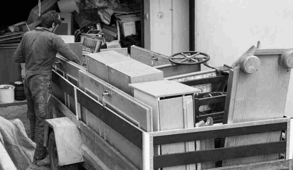 A man working with a large wooden or metal cabinet or structure in a workshop or garage, surrounded by various tools and materials.