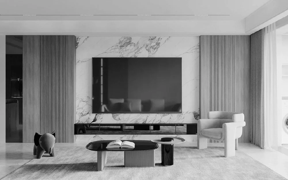 Modern living room with a flat-screen television mounted on a marble wall, a white armchair, a coffee table with an open book, and decorative objects, with large windows and curtains on the right side.