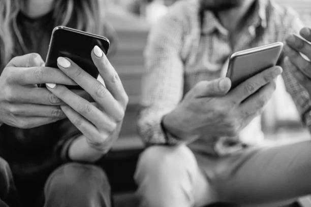 Two people sitting close together, each holding and looking at their smartphones.