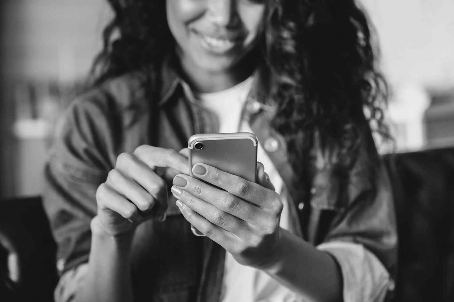 A woman with curly hair smiling while using a smartphone