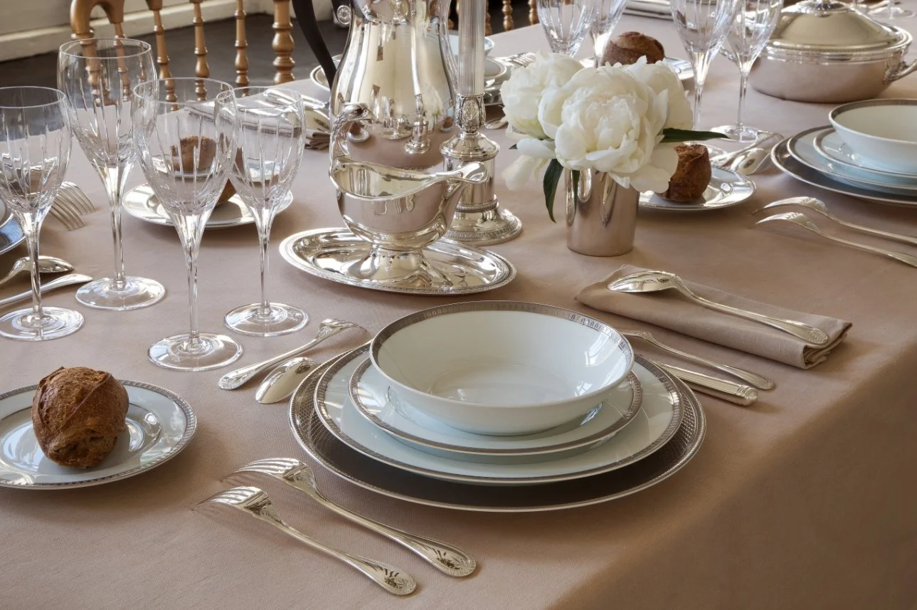 Elegant dining table set with white china, silverware, crystal glasses, a floral centerpiece, and floral napkins.