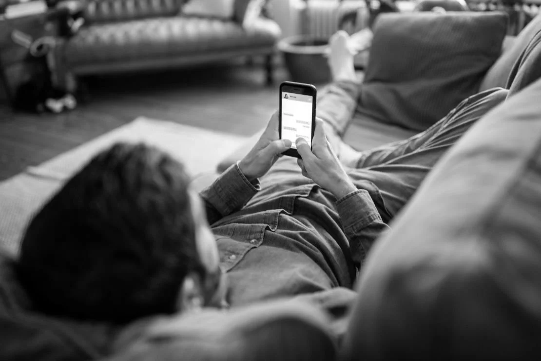 Person lying on a couch using a smartphone in a living room.