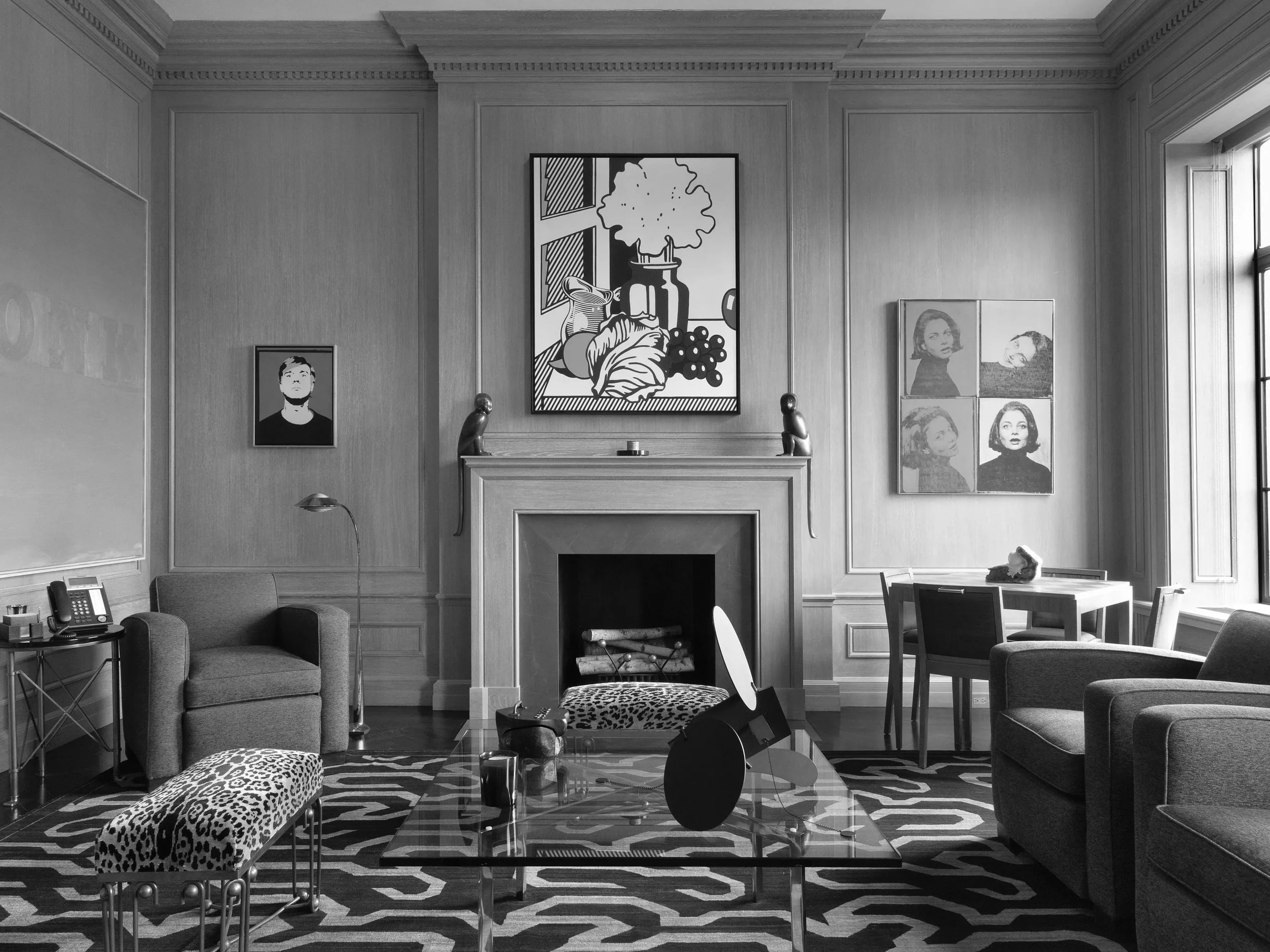 Living room with a fireplace, patterned rug, modern art on the walls, a glass coffee table, and various chairs and sofas.
