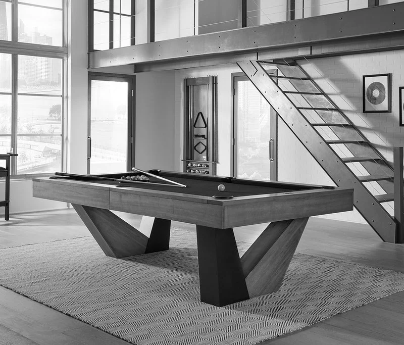 Modern indoor space with a pool table, staircase, large windows, and city skyline view.