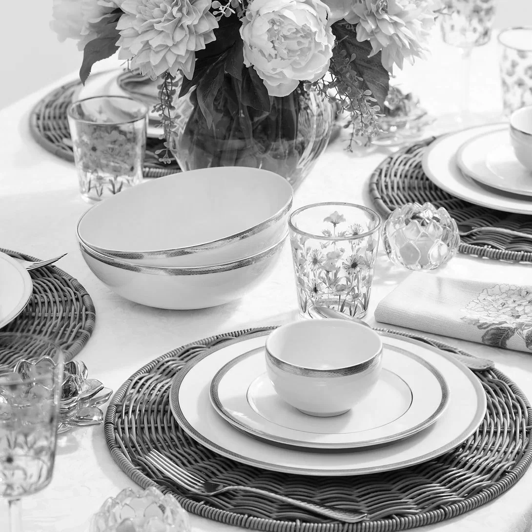 A table set with various plates, bowls, glasses, napkins, and a floral centerpiece in a vase, arranged for a meal.