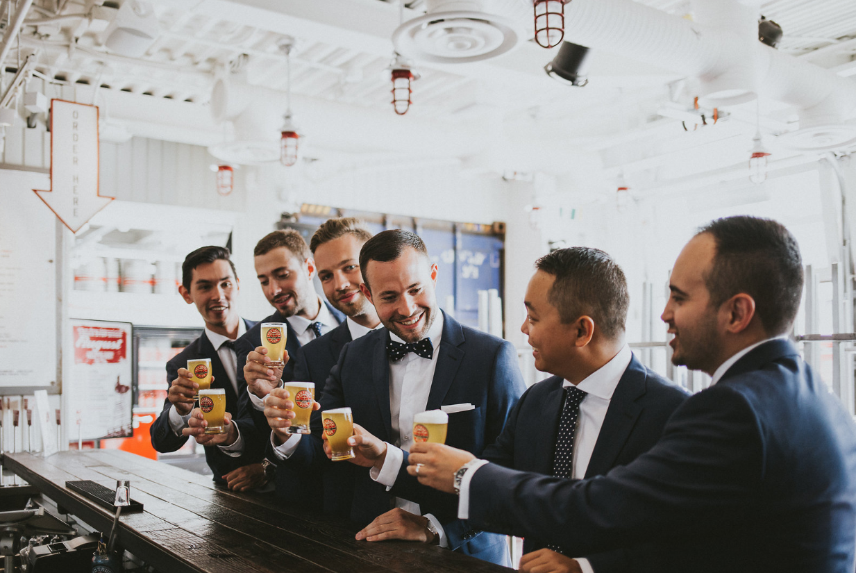 Six men in suits and ties enjoying drinks at a bar, smiling and chatting.