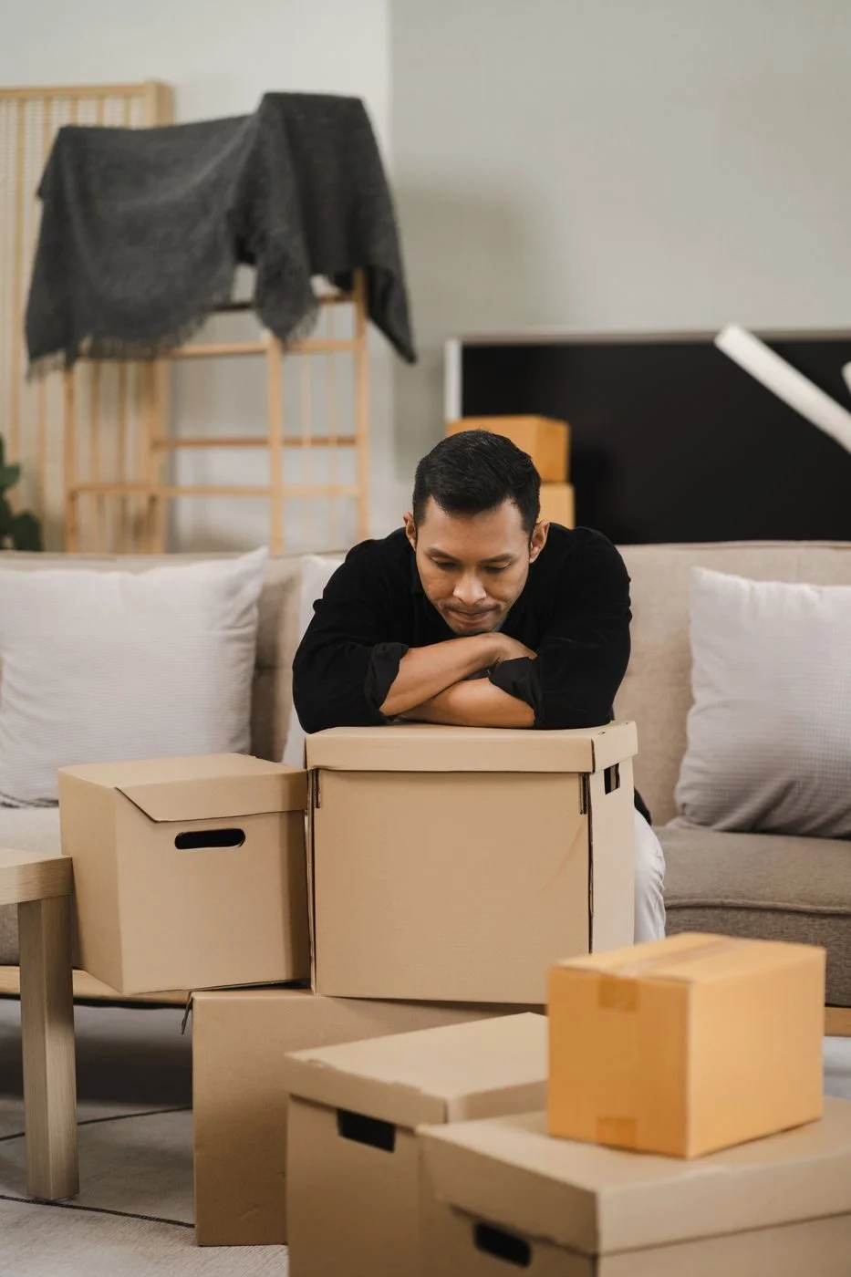 man leaning on moving boxes looking sad because he is dealing with a divorce