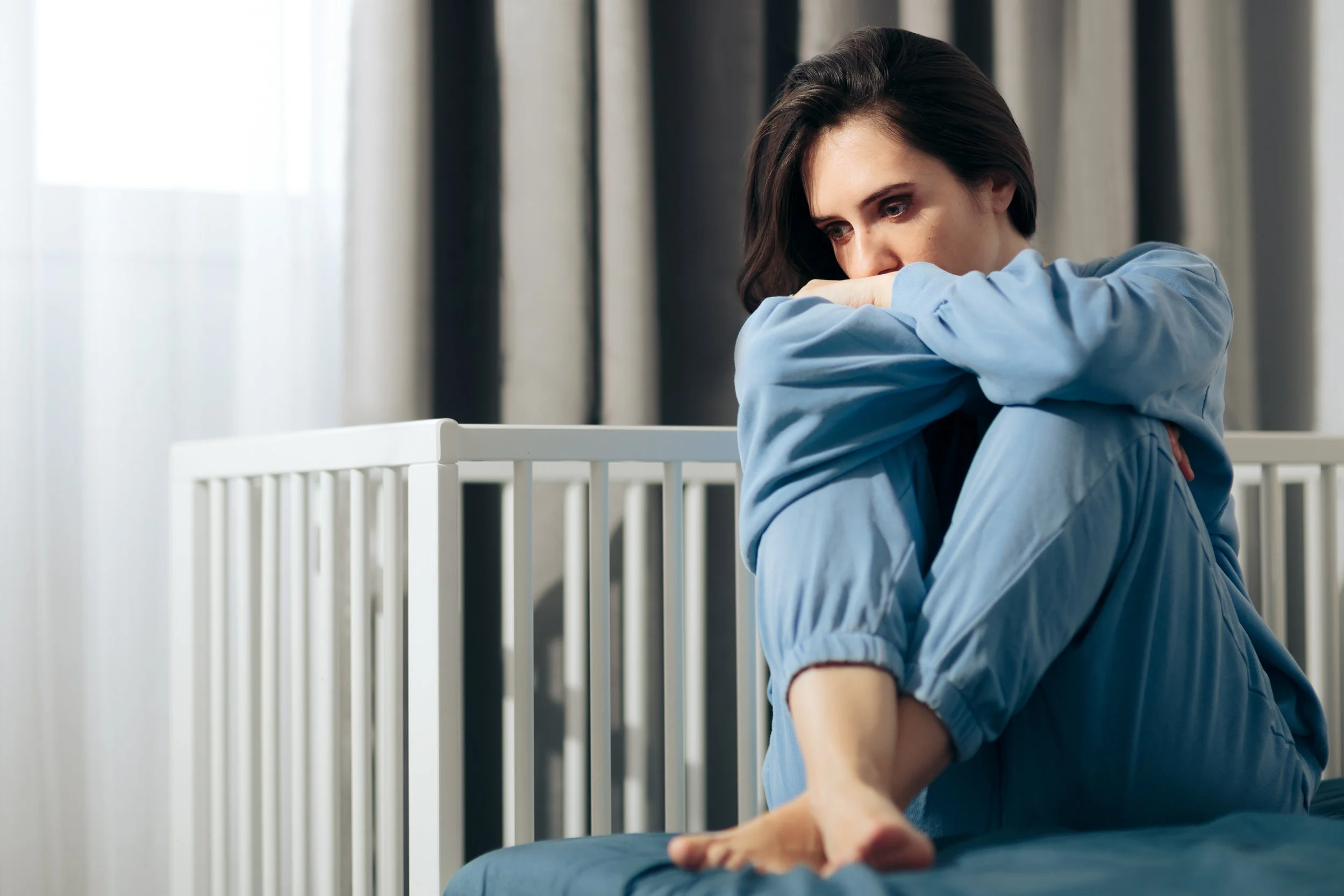 woman with postpartum depression sitting by crib crying, postpartum anxiety vs postpartum depression