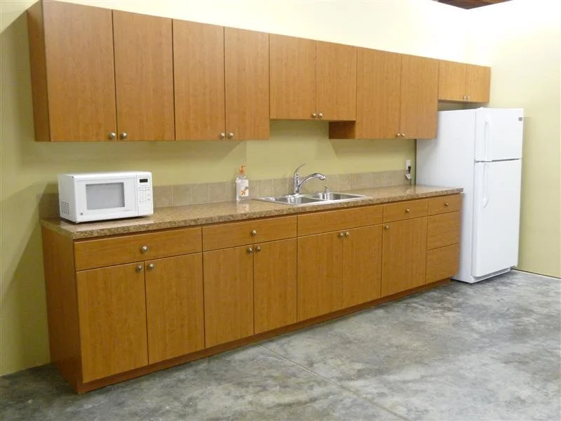 Kitchen area with wooden cabinets, a microwave, a soap dispenser, a sink, and a white refrigerator.