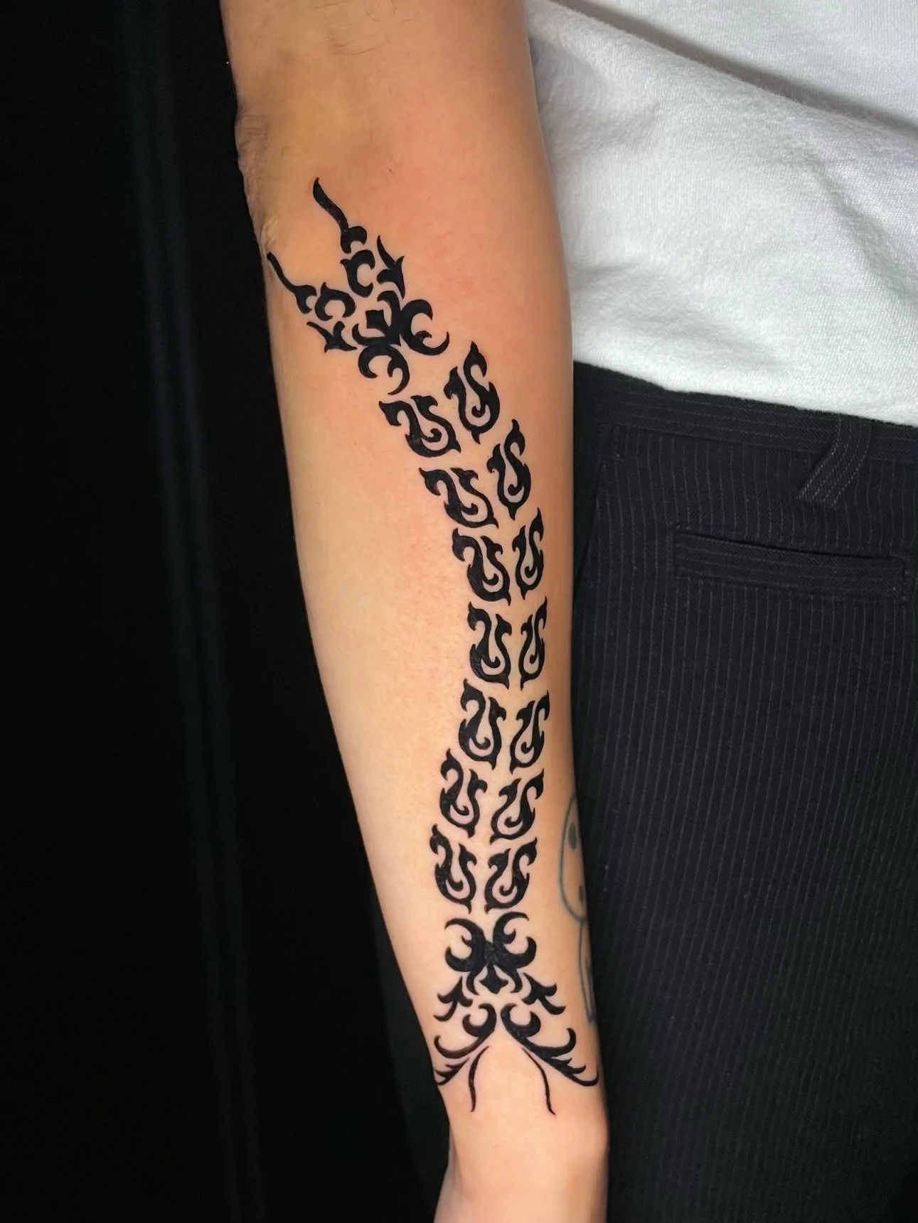 Bold blackwork ornamental forearm tattoo featuring intricate tribal-inspired patterns, repeating abstract symbols, and flowing decorative flourishes extending from the elbow to the wrist—tattoo by Hayden Herndon at Cloak Collective.