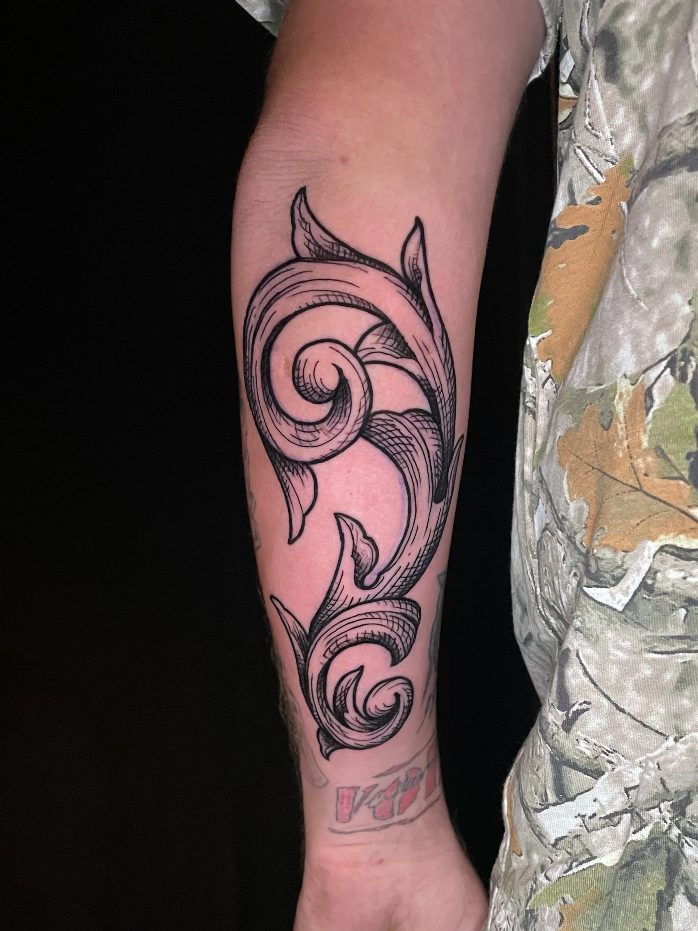 Intricate blackwork ornamental forearm tattoo featuring bold swirling filigree, elegant scrollwork, fine line details, and crosshatch shading inspired by traditional decorative engraving—tattoo by Hayden Herndon at Cloak Collective.