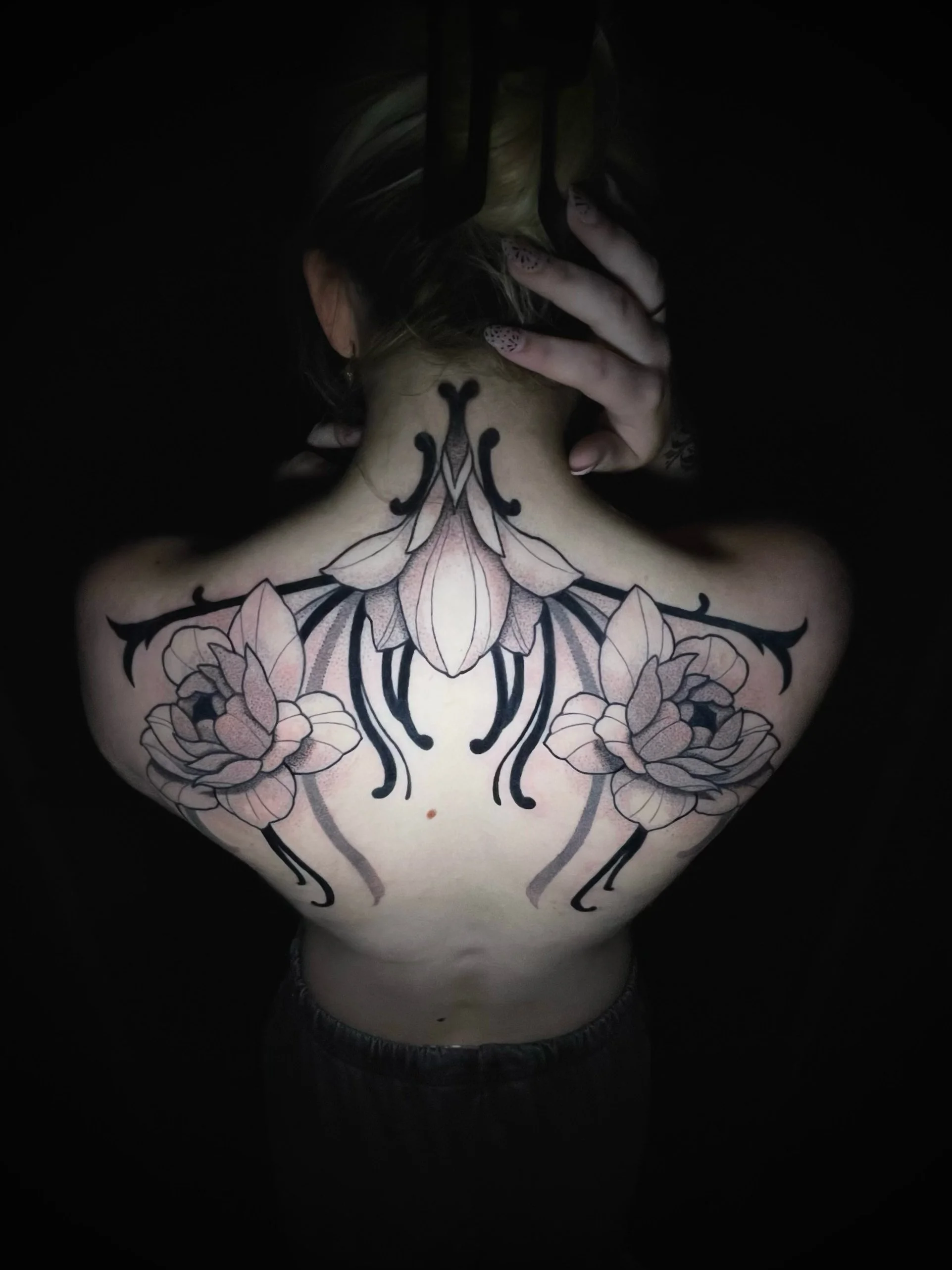Ornamental black and gray upper back tattoo featuring symmetrical floral designs, delicate dotwork shading, and flowing decorative linework extending across the shoulders and neck—tattoo by Hayden Herndon at Cloak Collective.