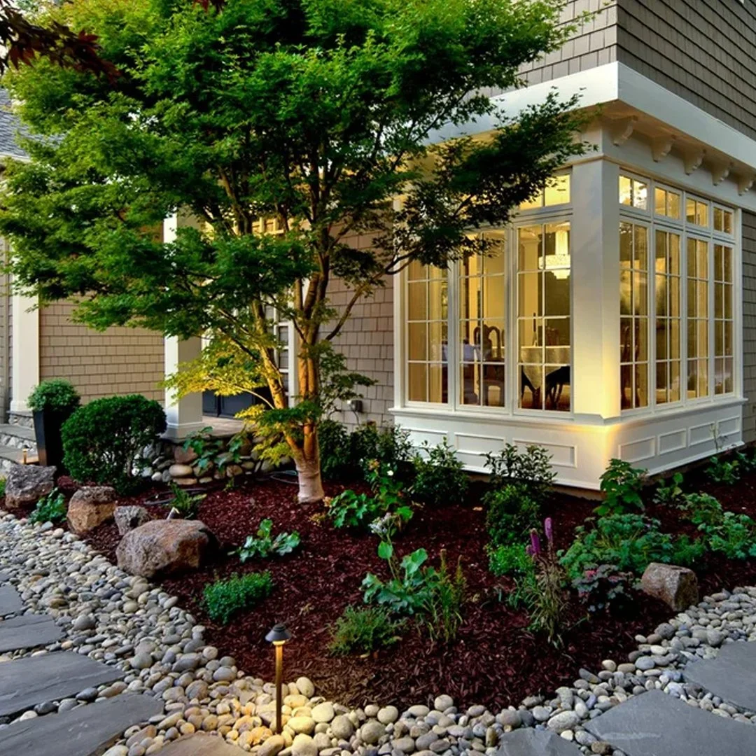 A vibrant, fully established garden with mature flowering plants and lush trees frames a residential home, showcasing the long-term value of a mature landscape.