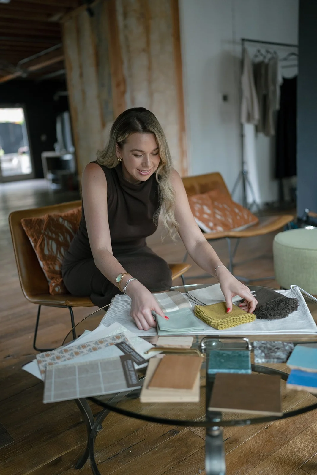 A woman selecting fabric swatches and materials for interior design or home decor at a glass table in a modern, stylish room.