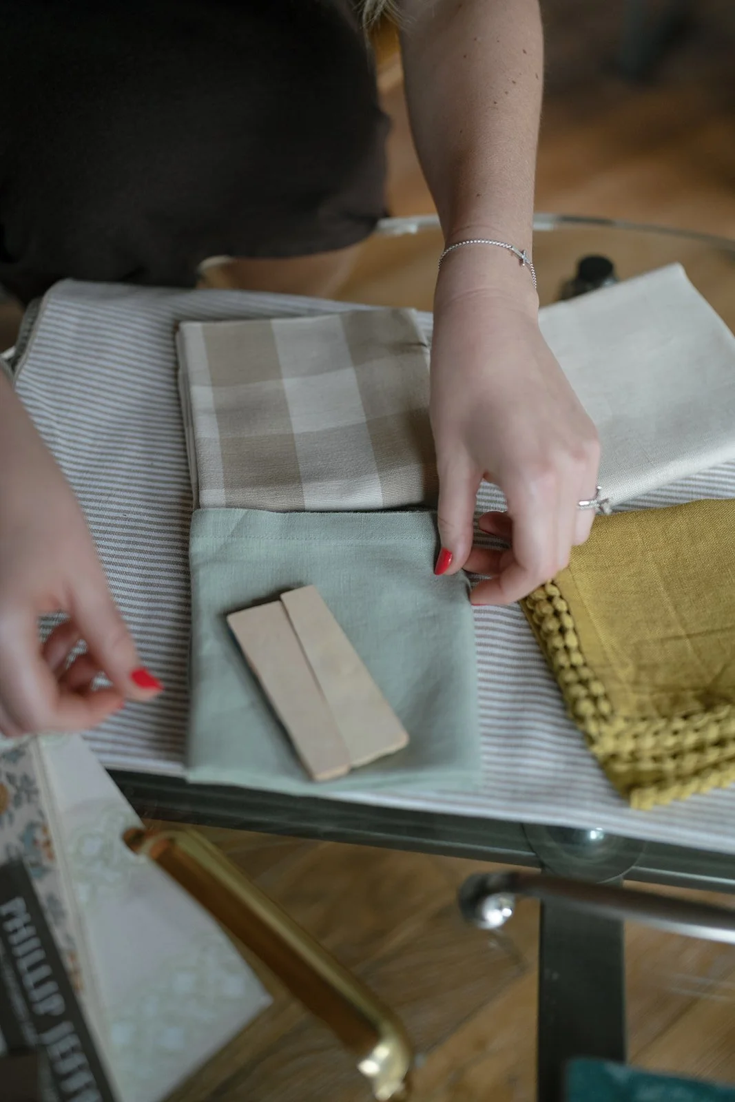 Person with red nail polish shows fabric samples and swatches on a table.