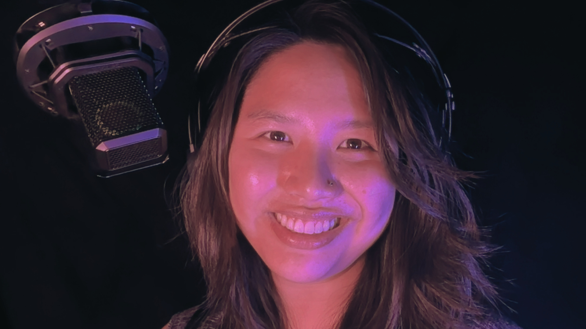 Ashley Duongtran, audiobook narrator, in her recording booth wearing headphones with microphone in frame