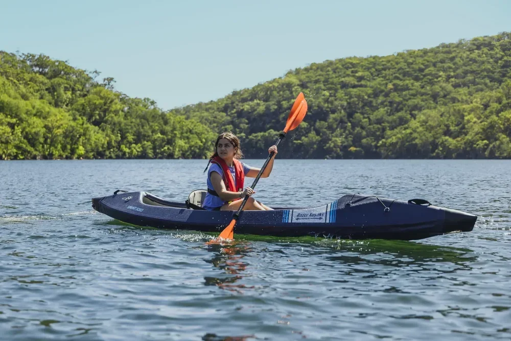 Frau beim Paddeln in einem Razor Kayaks Sprint Solo Schlauchkajak auf einem See mit grünen Hügeln.