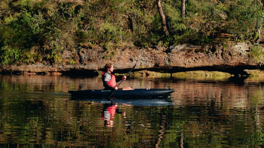 Paddler in einem Razor Kayaks R1 Ultra Schlauchkajak auf ruhigem Wasser nahe einem bewaldeten Ufer.