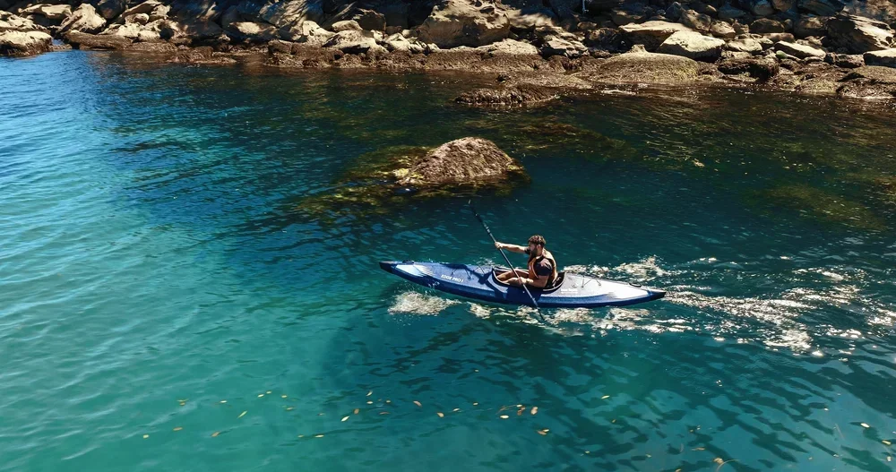 Paddler in einem Razor Kayaks Edge Pro 1 Schlauchkajak auf klarem Wasser nahe einer felsigen Küste.