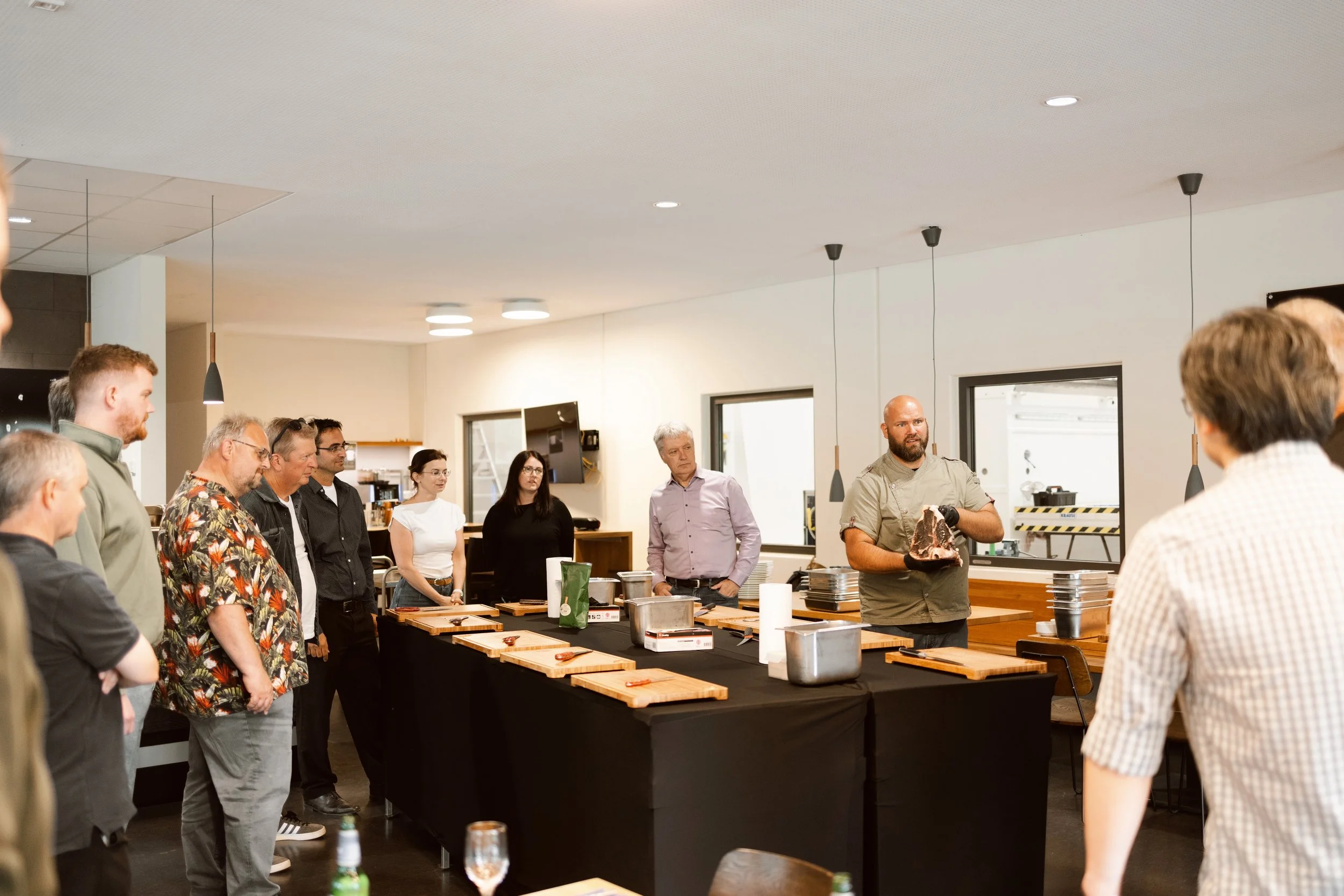 Ein Koch erklärt einer Gruppe von Menschen im Restaurant, wie man ein Stück Fleisch schneidet.