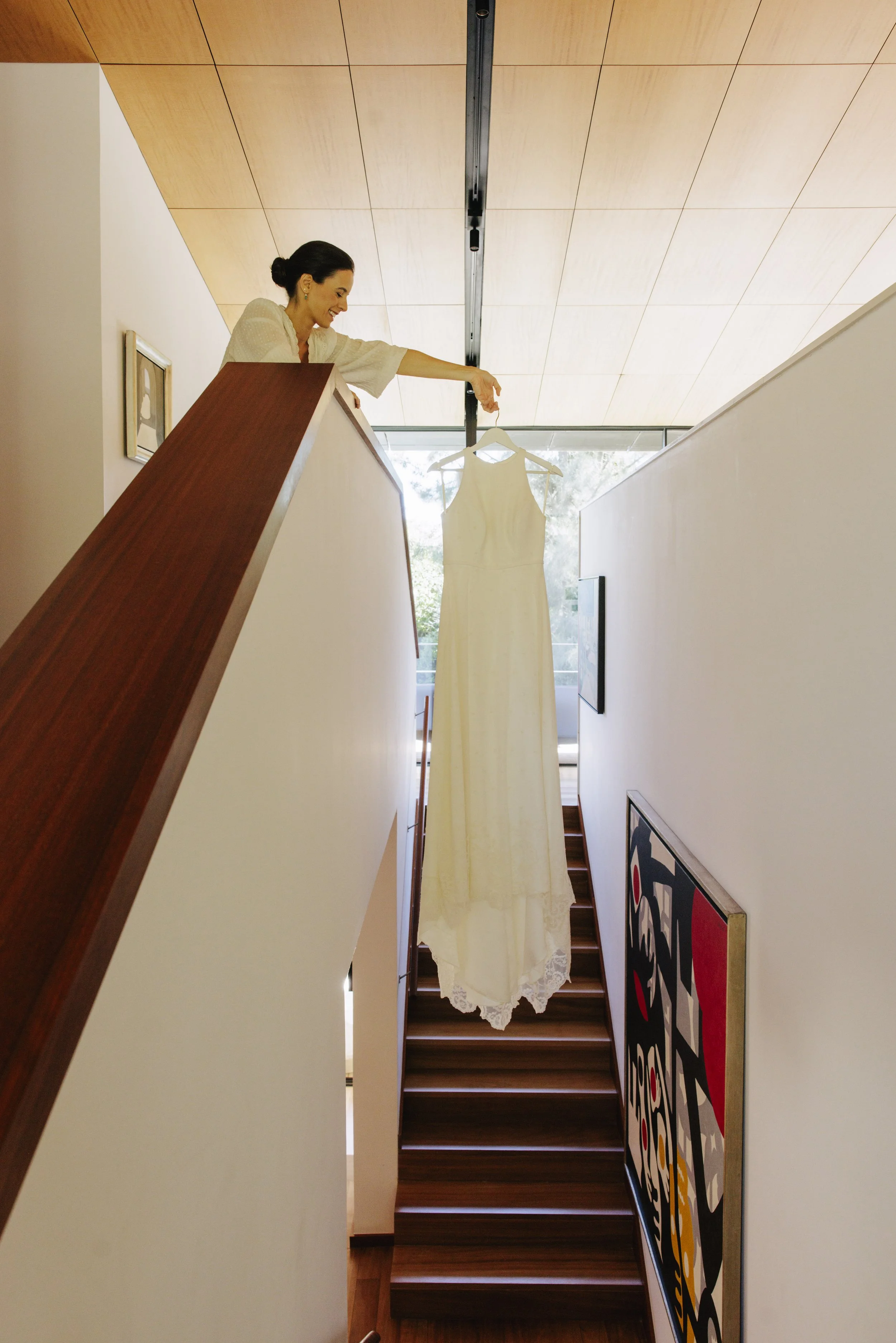 Woman on stairs holding a white dress on a hanger, with colorful modern artwork on the wall.