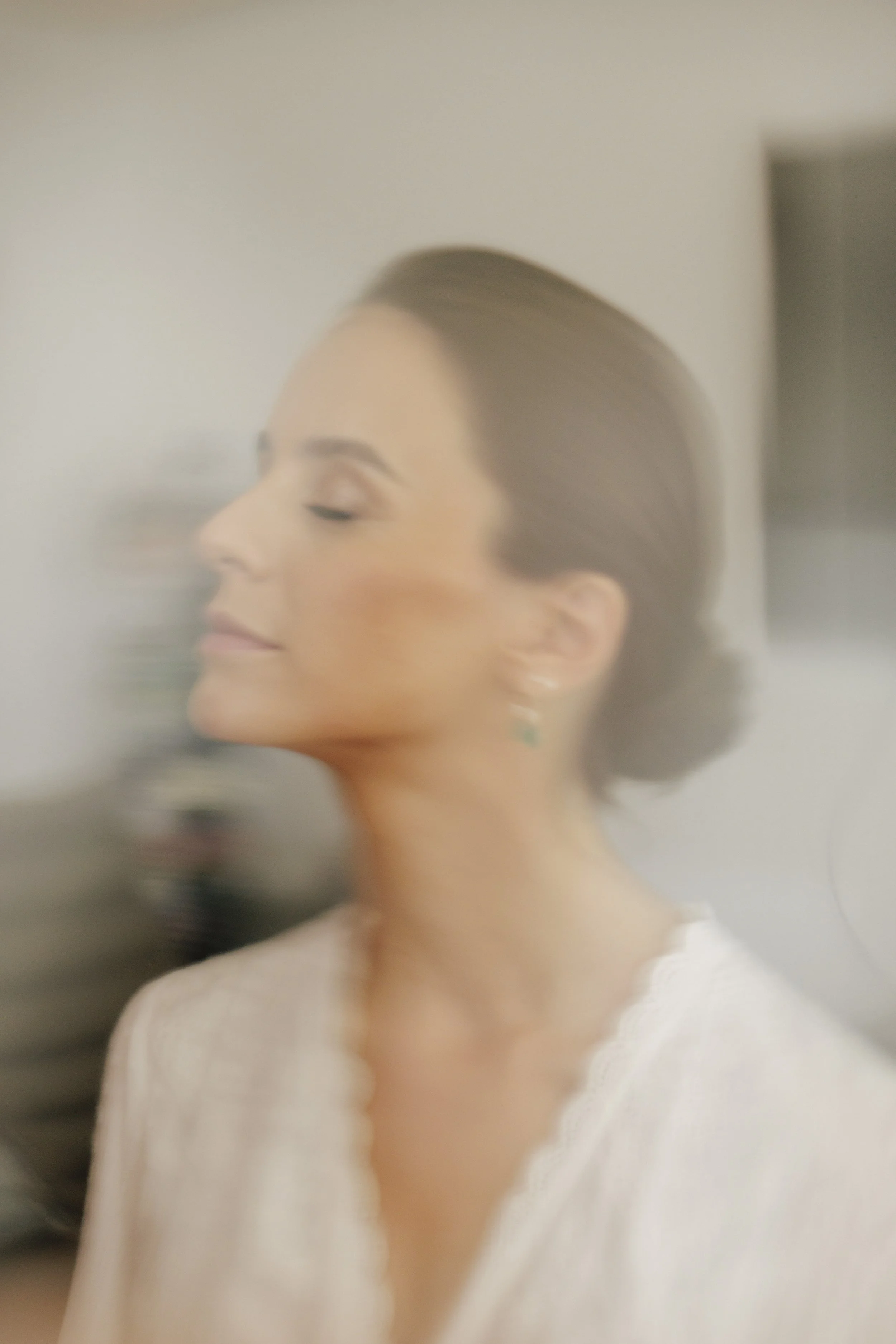 A woman with closed eyes, brown hair tied back, wearing earrings, in a white off-the-shoulder top, appears to be relaxing with a calm expression.