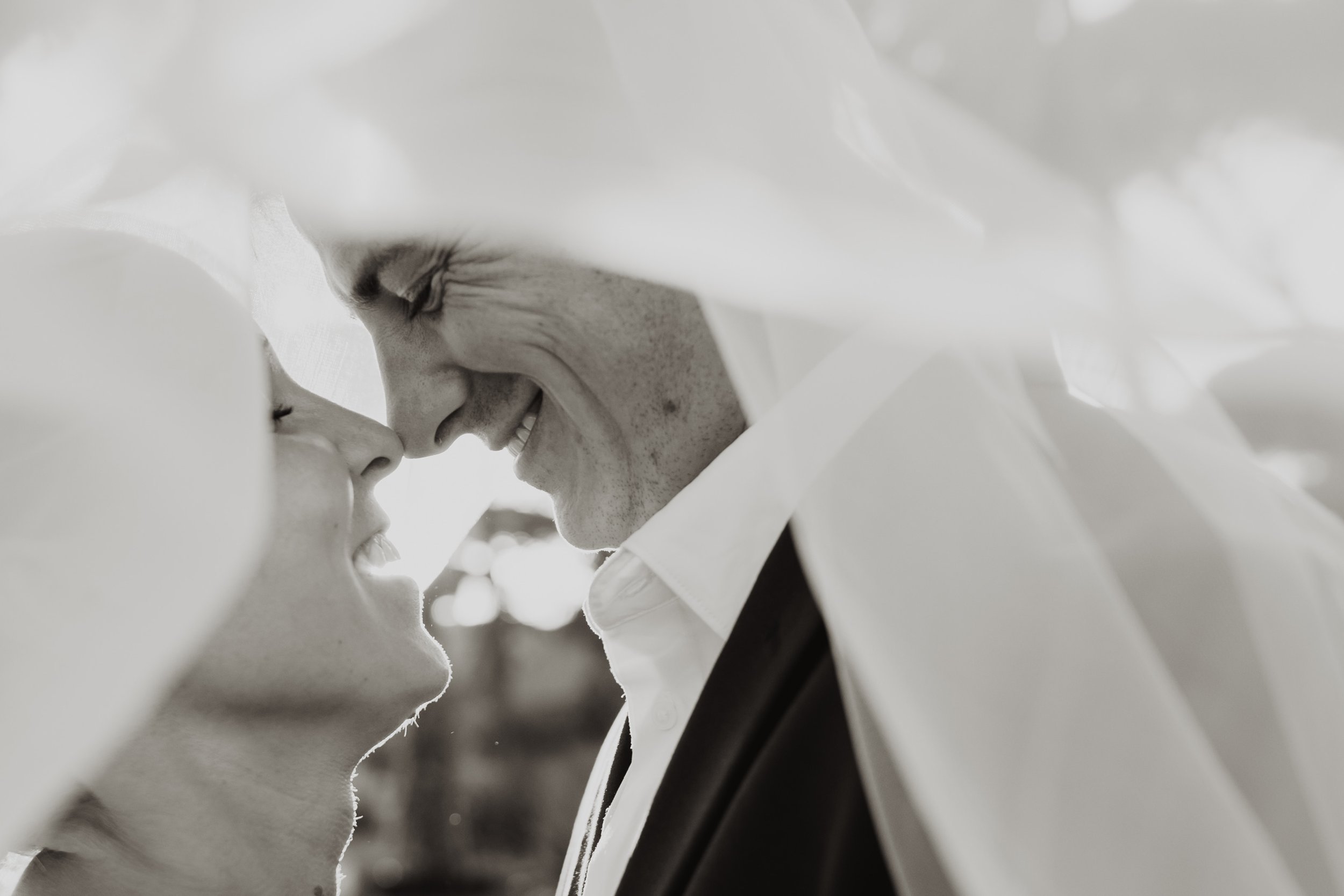 Two white ceramic figurines of a couple about to kiss, partially hidden behind white tissue paper.