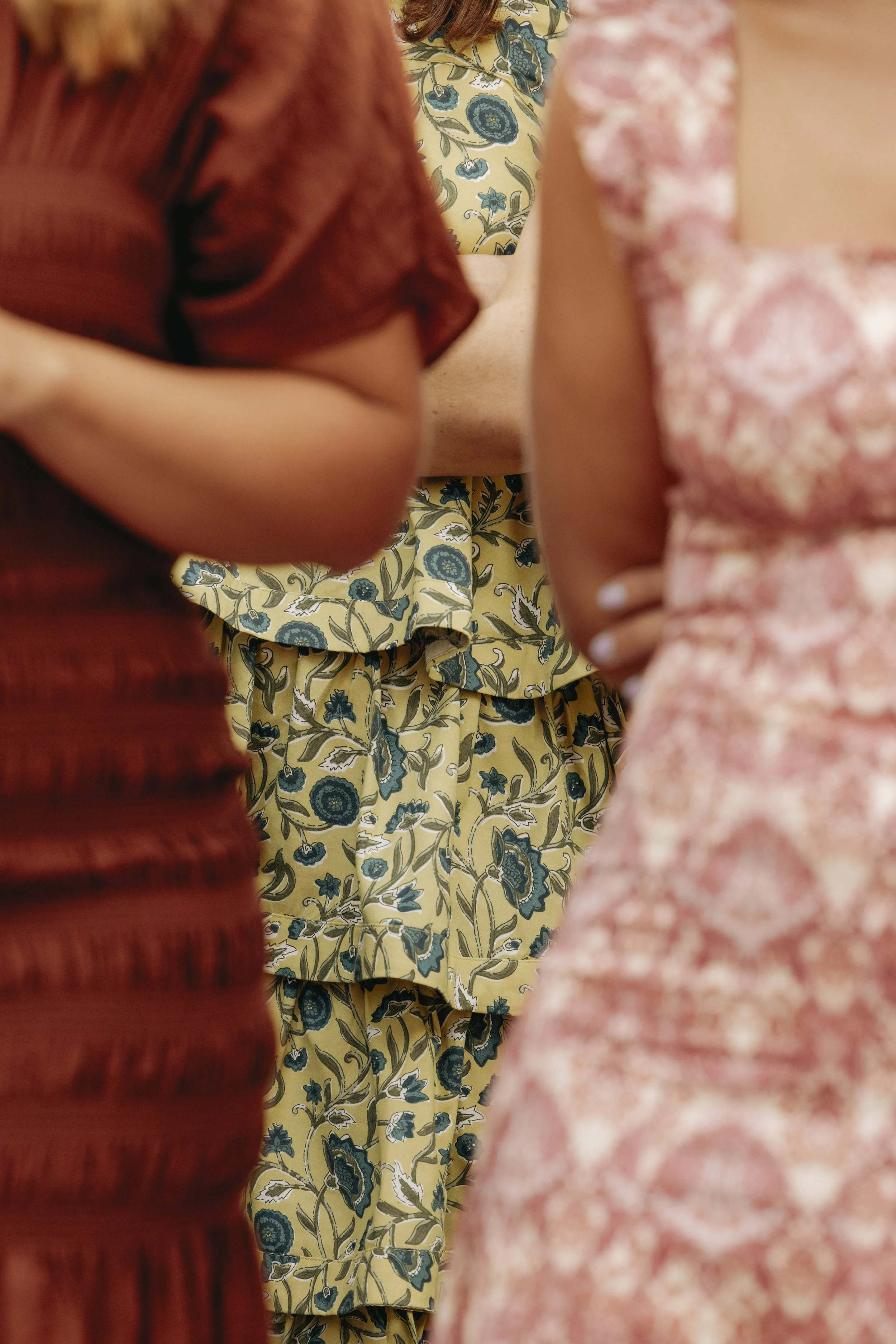 Close-up of three women in floral dresses, standing closely together, with one woman in the center wearing a yellow dress with blue floral patterns.