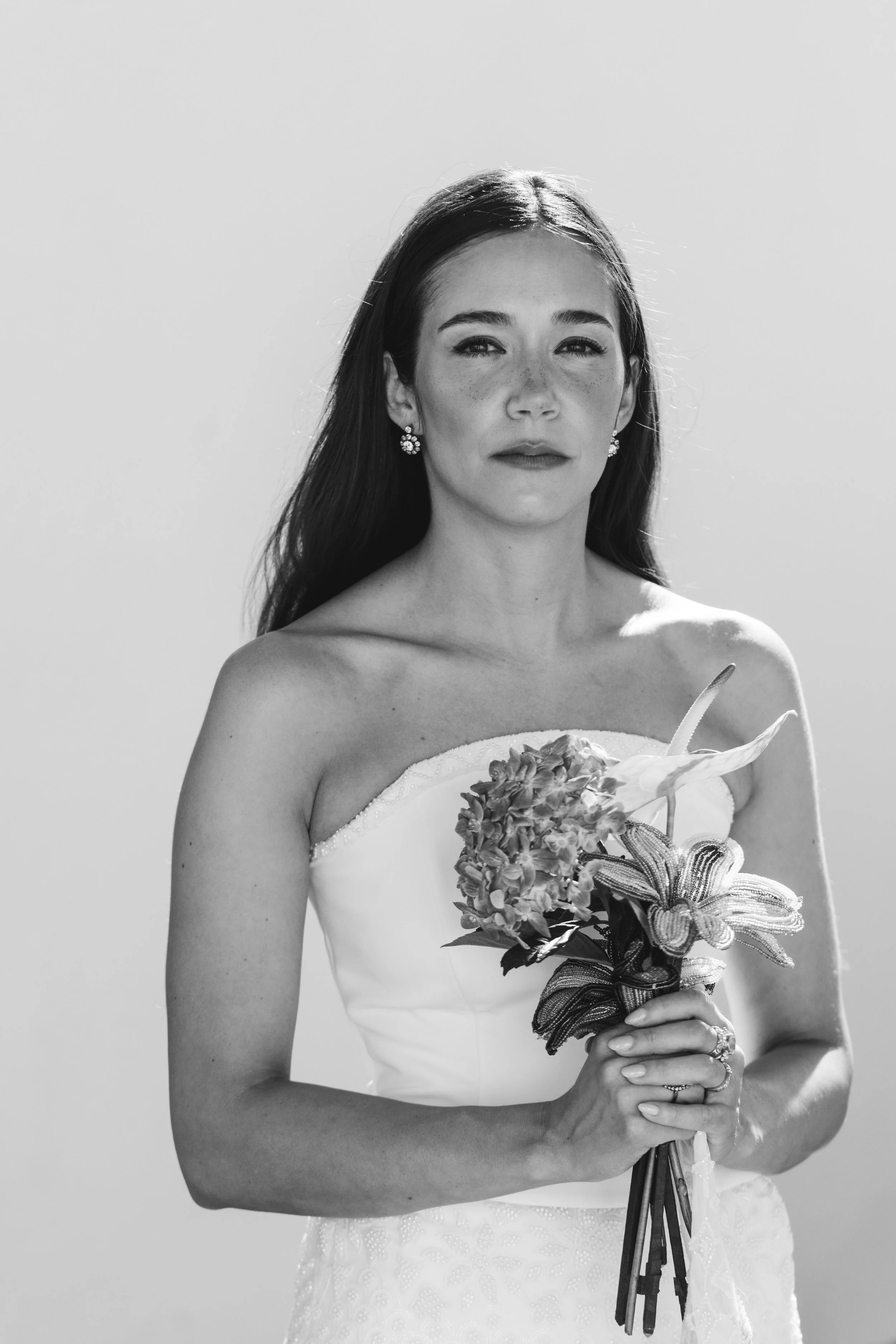 Black and white photo of a woman in a strapless wedding dress holding a bouquet of flowers.